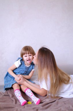 Küçük kızı öpüşme ve yatağın üstüne oturan genç anne.