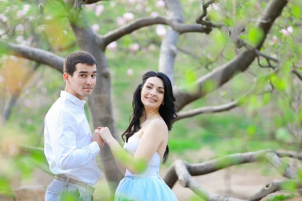Молода щаслива жінка і брюнетка чоловік обіймається біля квітучого дерева . — стокове фото