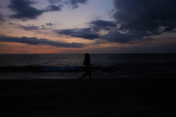 海と夕日を背景に黒いシルエットが女性を実行します。. — ストック写真