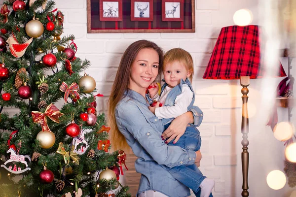 Joven madre caucásica de pie con su hija pequeña cerca del árbol de Navidad . — Foto de Stock