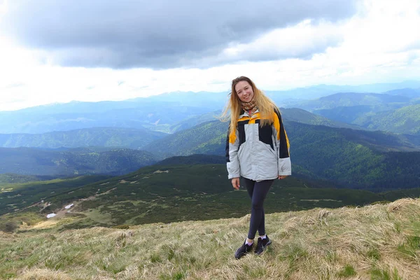 Jovem sorridente turista feminina vestindo casaco amarelo em pé nas montanhas dos Alpes . — Fotografia de Stock