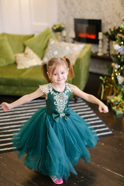 Kleines Mädchen in blauem Kleid steht neben Weihnachtsbaum. — Stockfoto