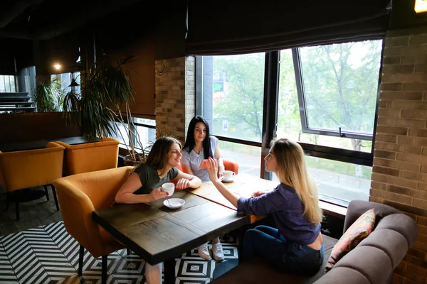 Vriendinnen spreken in café en het gebruik van smartphone, drinken koffie. — Stockfoto