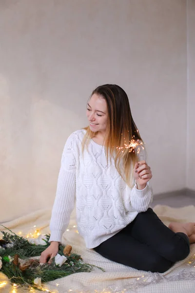 Jonge Kaukasische vrouw zitten met Bengalen licht in de buurt van twinkling gele slingers en groene krans. — Stockfoto