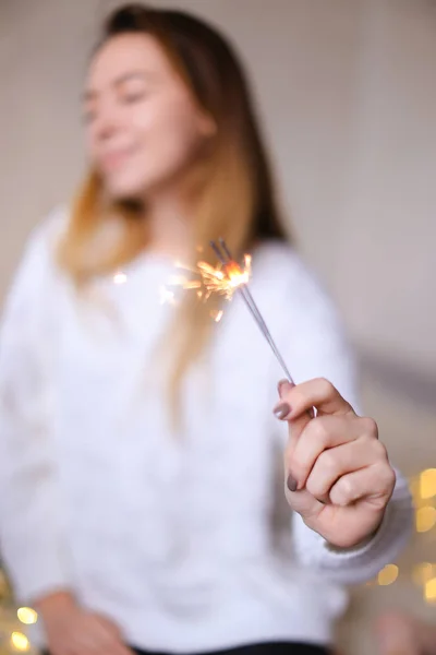 Foto sfocata di giovane donna felice seduta con primo piano luce bengala vicino scintillante ghirlande gialle . — Foto Stock