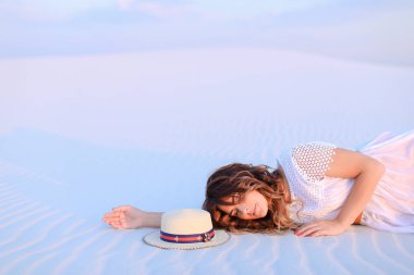 Şapka yakınındaki beyaz kum üzerinde yatan genç kadın insan.