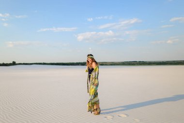 Kum üzerinde duran mayo ve plaj elbise giyen genç kadın.