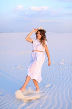 Beyaz elbise ve çölde kum tekme şapka giyen genç kadın.