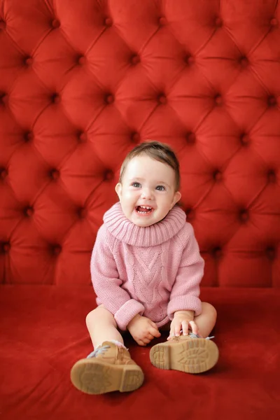 Little female baby sitting in red background on sofa. — Stock Photo, Image