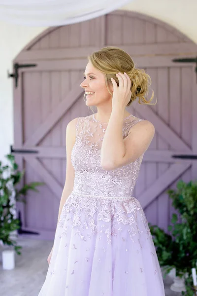 Όμορφη ξανθιά νύφη φοράει φόρεμα και στέκεται κοντά ξύλινη πύλη. — Φωτογραφία Αρχείου