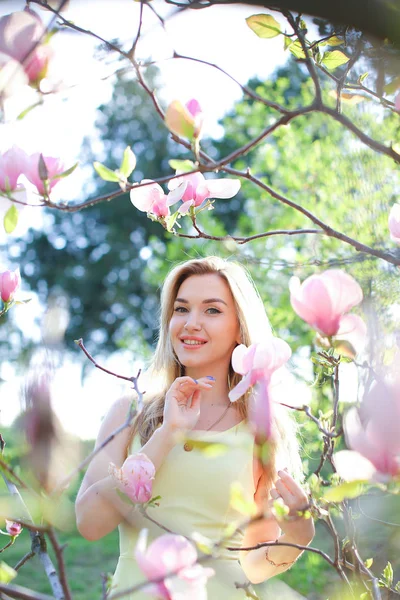 Unga leende kvinna som står nära magnolia i park. — Stockfoto