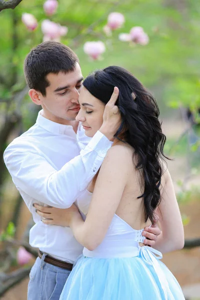 Jovem feliz mulher pessoa e morena homem abraçando perto de árvore florescendo . — Fotografia de Stock