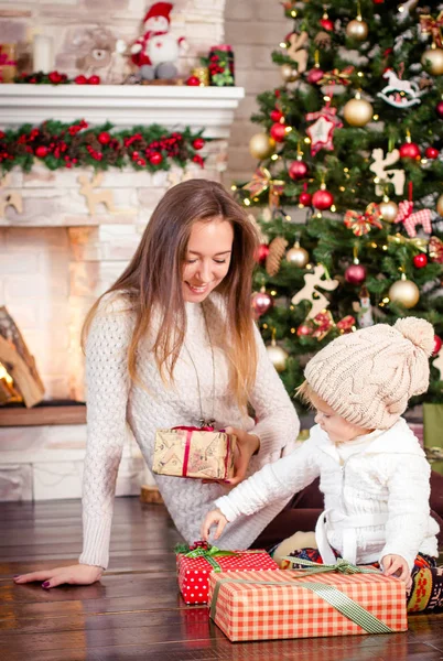 Jovem mãe caucasiana sentada com a pequena filha perto de lareira decorada e árvore de Natal . — Fotografia de Stock