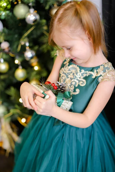 Kleines hübsches Mädchen mit Geschenkkleid, das neben dem Weihnachtsbaum steht. — Stockfoto