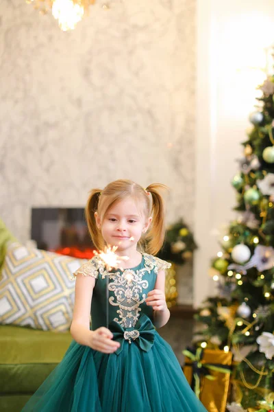 Kleines nettes Mädchen in Kleid und mit Bengalischen Lichtern am Weihnachtsbaum stehend. — Stockfoto