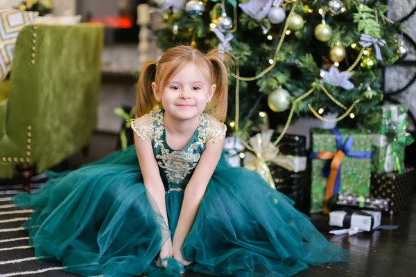Kleines schönes Mädchen in blauem Kleid, das neben dem Weihnachtsbaum steht. — Stockfoto