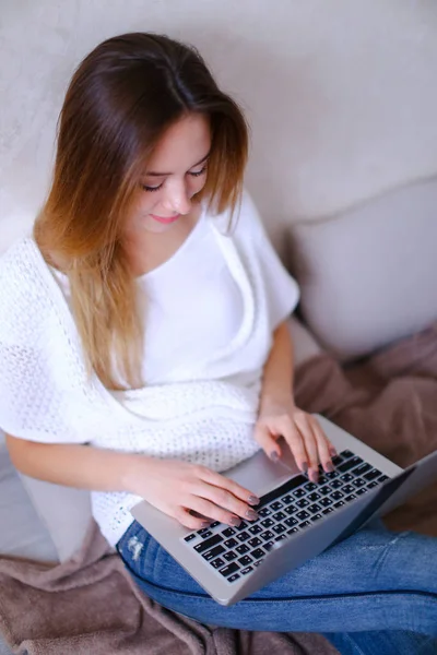 Chica joven trabajando con el ordenador portátil y sentado en la cama . — Foto de Stock