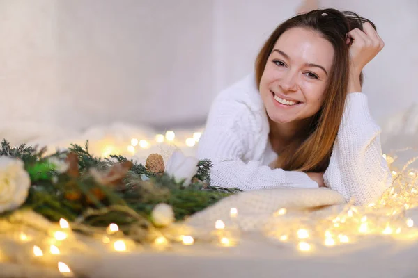 Jonge charmante vrouw liggend op bed in de buurt van de kroon van de groene en gele slingers. — Stockfoto