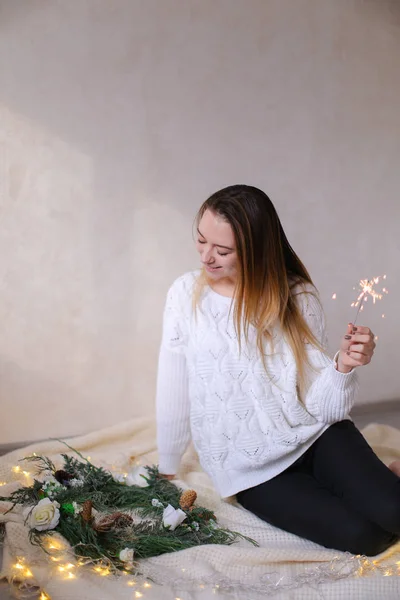 Gelukkig jongedame zitten met Bengalen licht in de buurt van twinkling gele slingers en groene krans. — Stockfoto