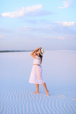 Beyaz elbise ve çölde kum üzerinde yürüyüş şapka giyen genç bayan