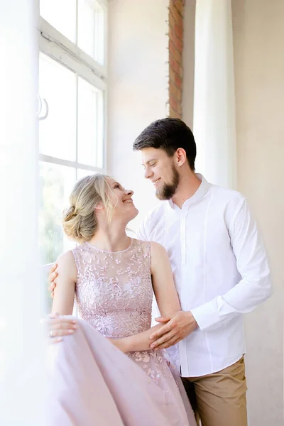 Blonda anbud bruden står nära fönster och brudgummen. — Stockfoto