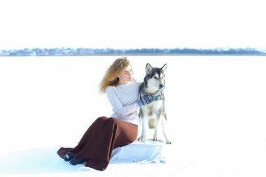 Beyaz kar arka planda husky ile oturan eldivenler giymiş kadın.