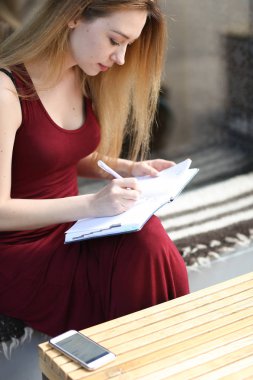Genç kız öğrencinin yazılı defter Üniversitesi'nde, tablo smartphone olarak.