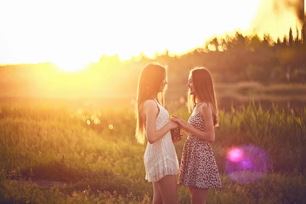 Jonge meisjes permanent op gras in de zonnestralen en hand in hand. — Stockfoto