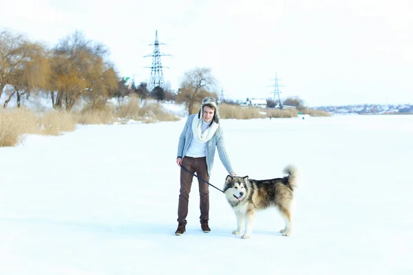 Człowiek sobie sweter, brązowy spódnica i rękawiczki, siedząc na śniegu i przytulanie pies husky. — Zdjęcie stockowe