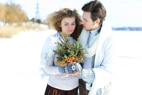 Hombre abrazando a mujer manteniendo ramas de abeto en fondo blanco de invierno . — Foto de Stock