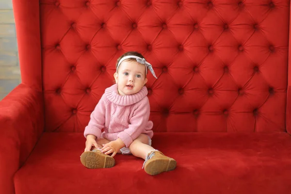 Kleines lächelndes Mädchen auf rotem Sofa. — Stockfoto