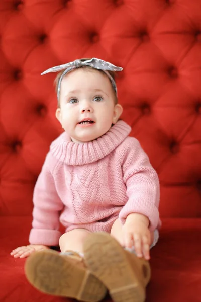 赤い背景のソファの上に座っている少しの幸せな女性の赤ちゃん. — ストック写真