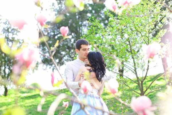 Genç kız ve esmer adam çiçek açan ağacın yanında sarılma. — Stok fotoğraf