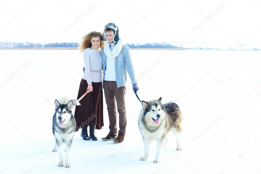 Woman and man walking with huskies in white winter background.