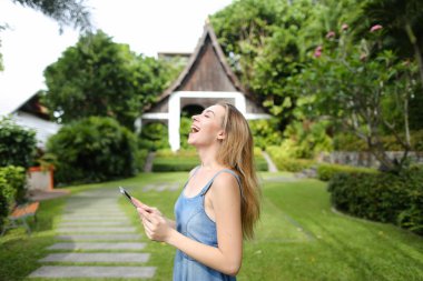 Smartphone kullanarak ve resort ev arka planda duran genç güzel kız.