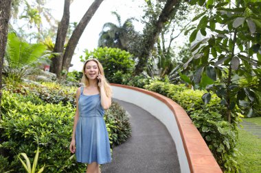 Kot sundress giyen genç beyaz kadın yanında smartphone yakınındaki tropik bitkiler, söz.