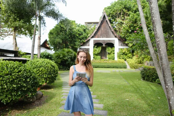 Smartphone kullanarak ve resort ev arka planda duran genç kadın.