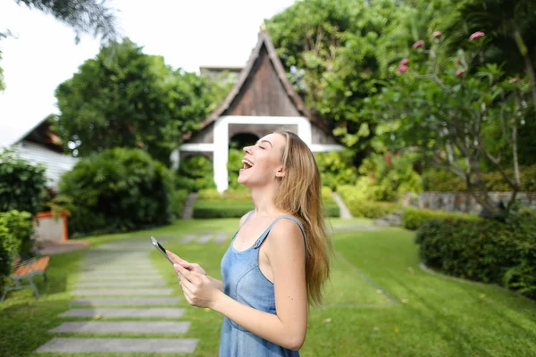 Smartphone kullanarak ve resort ev arka planda duran genç güzel kız.