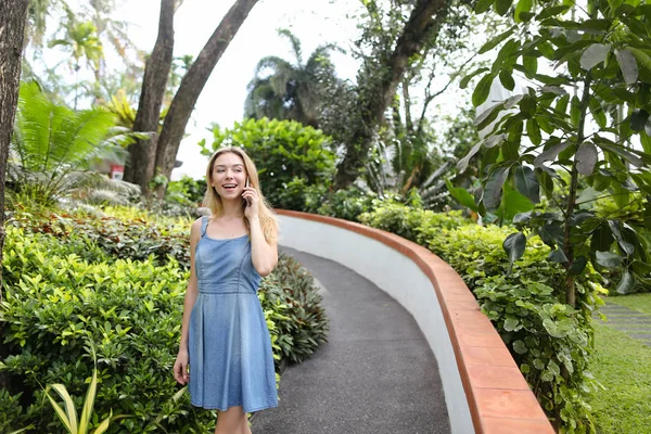 Kot sundress giyen genç beyaz kadın yanında smartphone yakınındaki tropik bitkiler, söz.