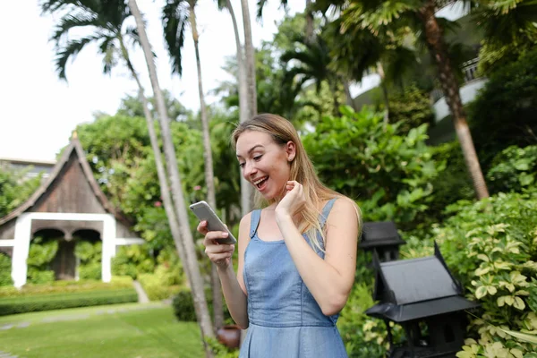 Kot sundress giyen smartphone ağaçlar, Bahçe içinde tarama kadın genç güzel.