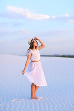 Beyaz elbise ve şapka kumsalda yalınayak gidiş genç bayan.