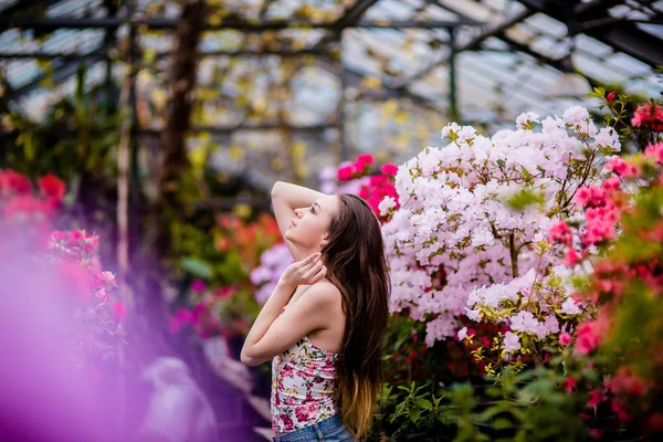 Jonge vrouw in de broeikas in de buurt van bloemen in het voorjaar. — Stockfoto
