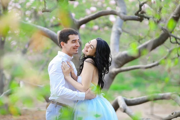 Young smiling woman and brunette man hugging near blooming tree. — Stock Photo, Image