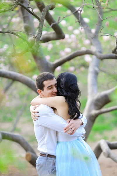 Jovem senhora e morena homem abraçando perto de árvore florescendo . — Fotografia de Stock