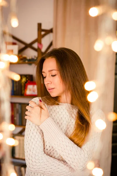 Jonge vrouw stond in de buurt van geel twinkling slingers op kamer. — Stockfoto