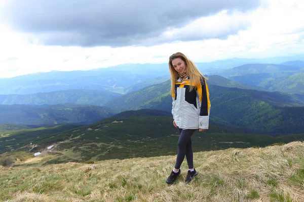 Junge Touristin in gelber Jacke steht in den Bergen der Alpen. — Stockfoto