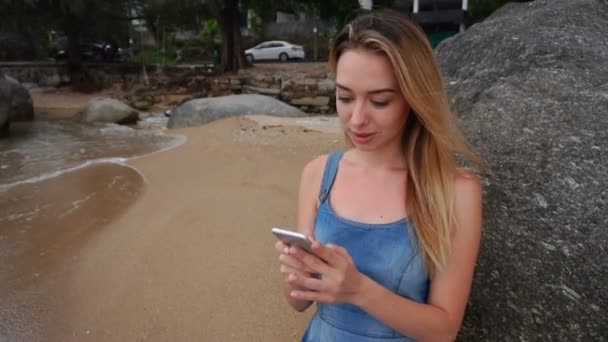 Медленная фотограф леди с помощью смартфона, чтобы поболтать на берегу моря — стоковое видео
