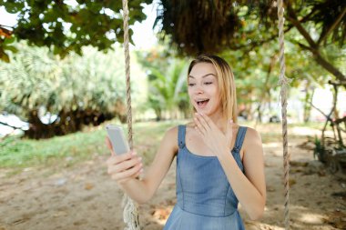 Salıncak kum üzerinde smartphone kullanmasına ve sosyal ağlar, Genç neşeli kız sürme.