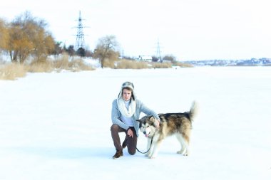 Kazak, kahverengi etek giyen adam ve kar üzerinde oturan ve sarılma mittens husky köpek.