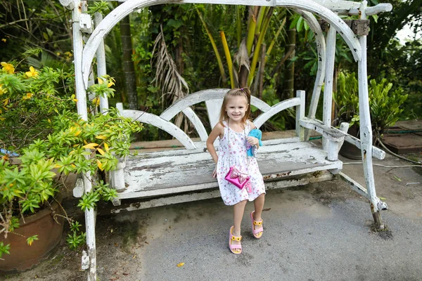 Joven niña agradable montar en columpio en jardín exótico, palmeras en el fondo . — Foto de Stock